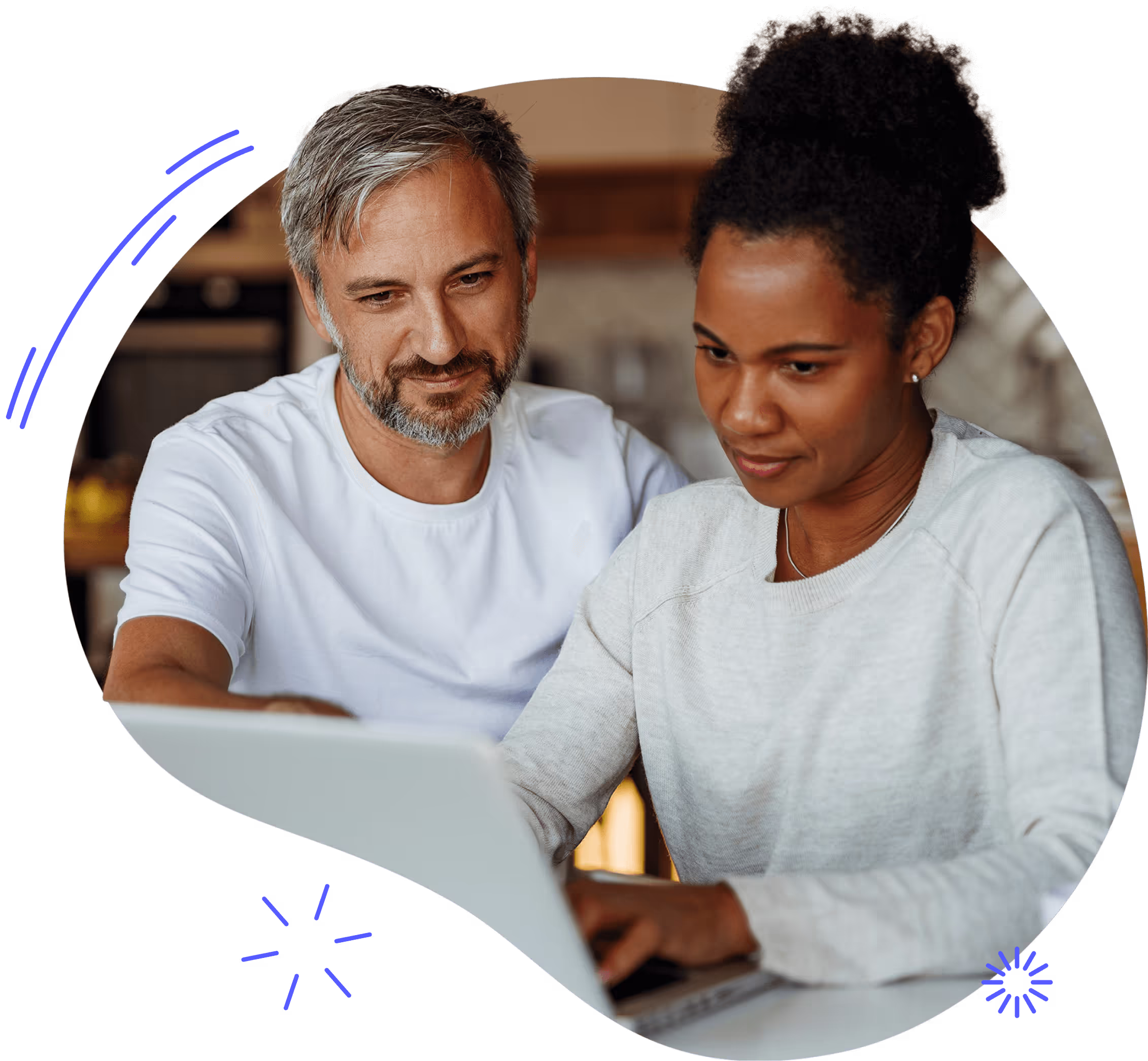 A couple sitting at a kitchen counter looking at a laptop together